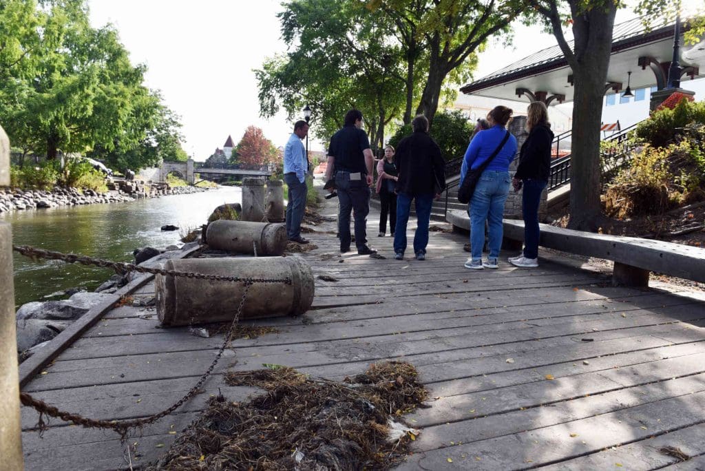people on a walkway next to a river that is covered in debris after flooding