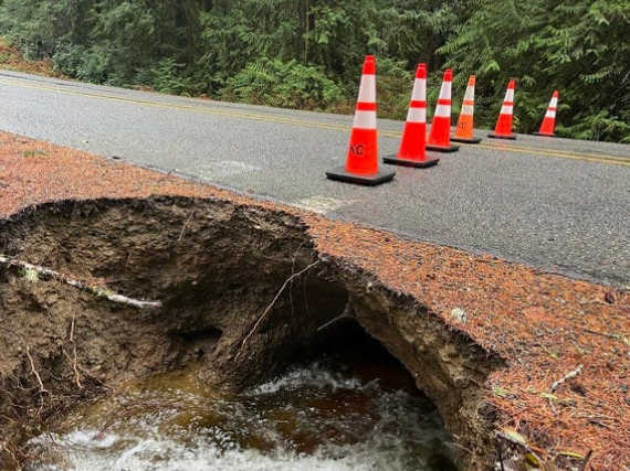 A large sinkhole under a road covered with cones to prevent traffic
