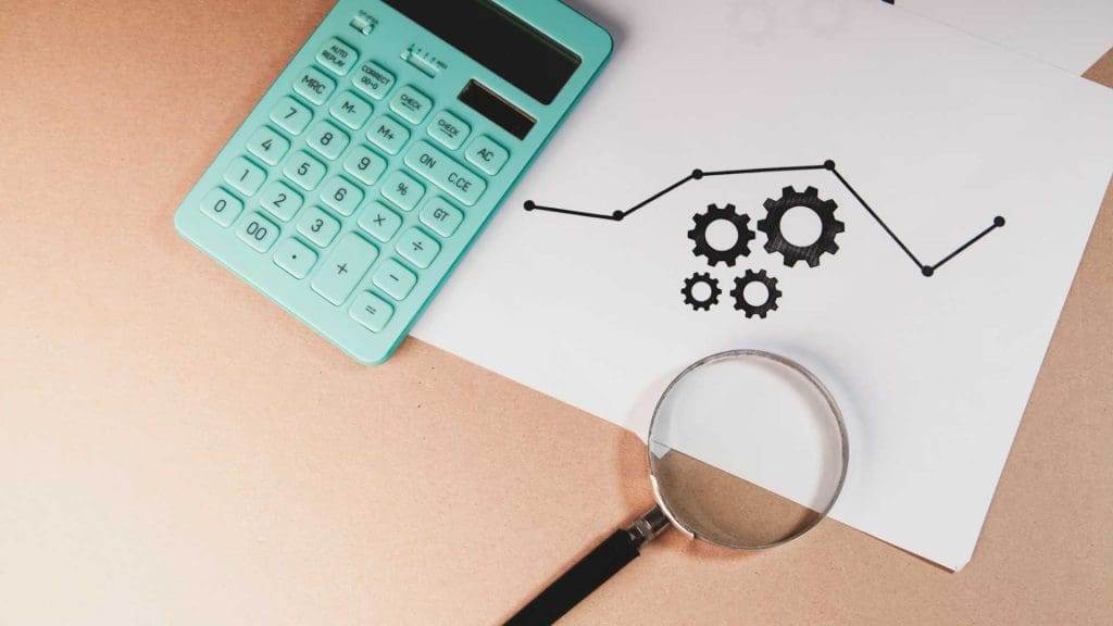 A calculator and a magnifying glass on a desk next to a printout of an upward graph