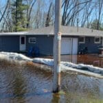 A flooded Wisconsin home surrounded by water and sandbags along a river.