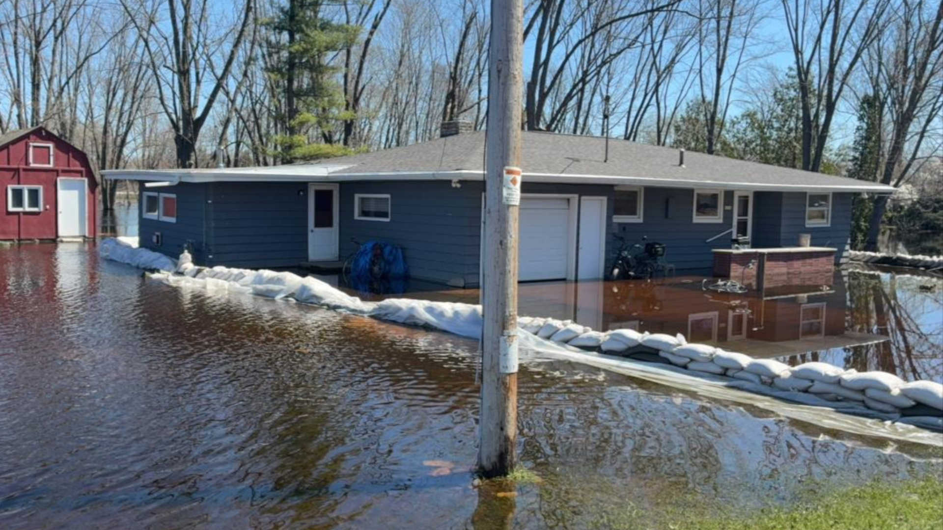 A flooded Wisconsin home surrounded by water and sandbags along a river.