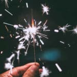 Someone holding a sparking sparkler firework in their hand.