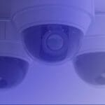 Three security cameras on a ceiling covered in a blue hue via photo editing.