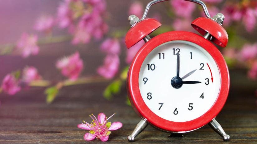 A clock indicating spring forward surrounded by flowers